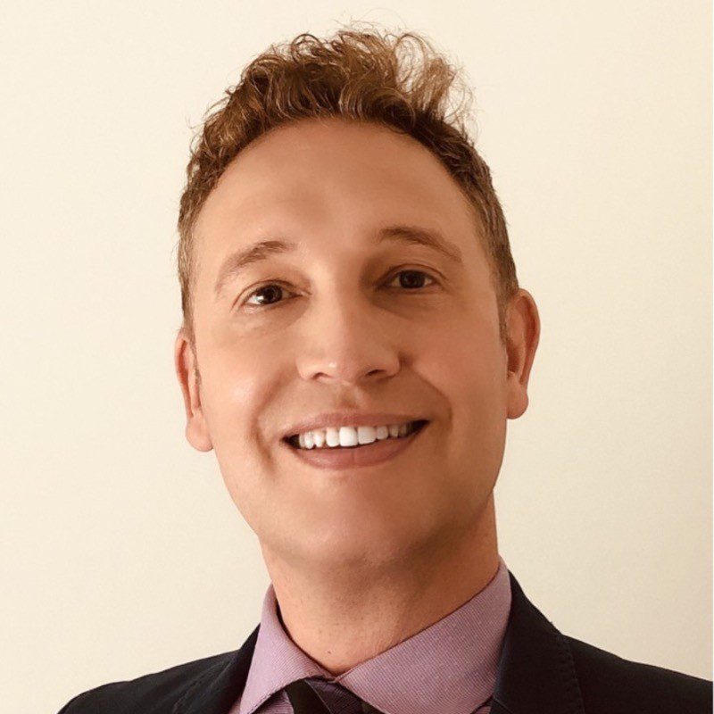Smiling man in business attire against a plain background.